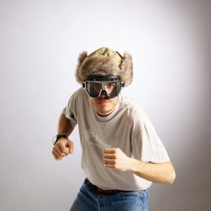 Studio portrait of Edoardo Melchiori wearing jeans, T-shirt, a furry heat and vintage motorbike goggles.
