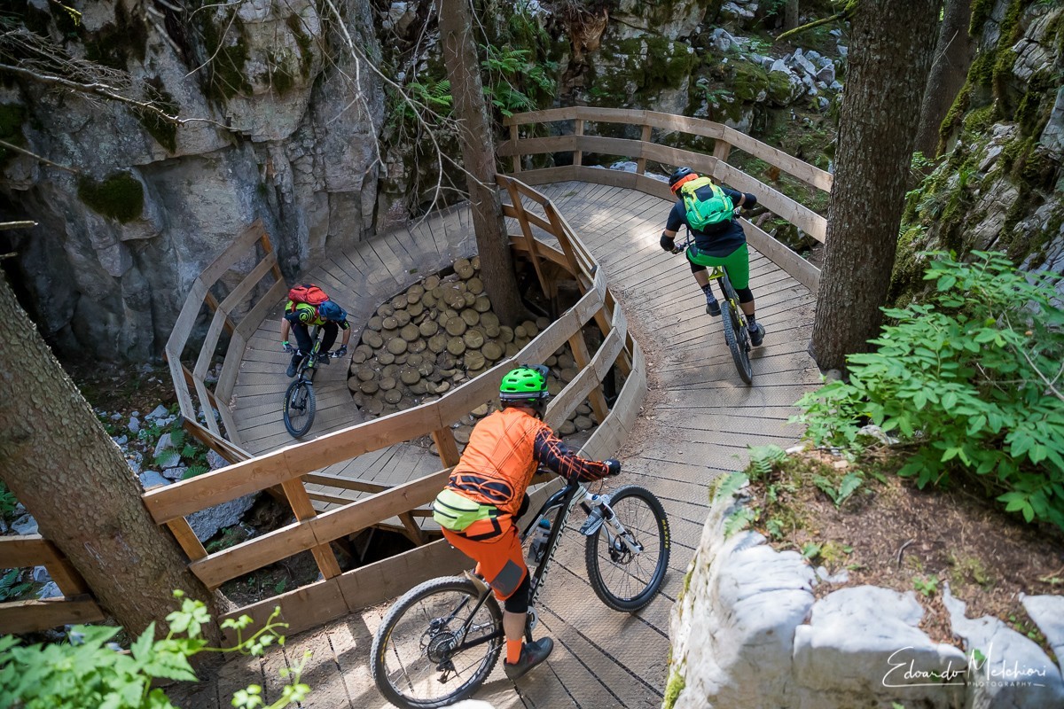 Three mountain bikers riding a wooded man made structure in the Dolomiti Paganella bike park